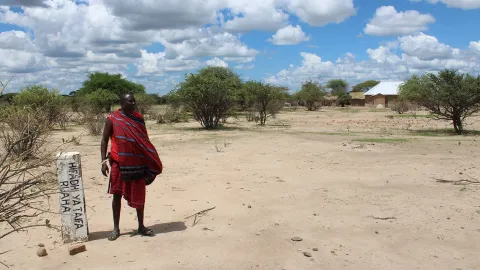 A Maasai pastoralist stands beside a beacon marking expansion of Ruaha National Park to consume his village and make communities trespassers in their own lands © The Oakland Institute