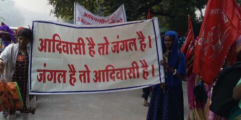 Women holding banner reading in hindi, "If there are forests, there will be Adivasis. If there are Adivasis, there will be forests." Credit: Oakland Institute